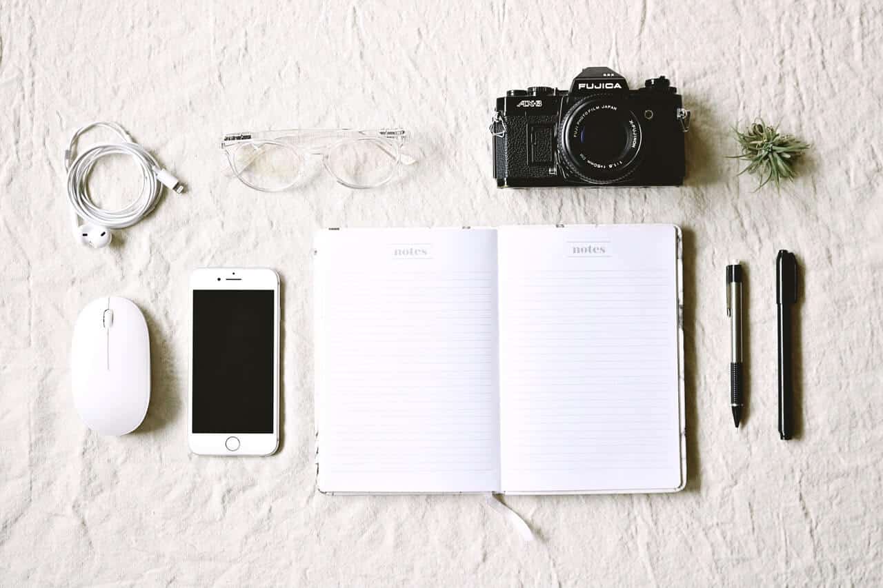 white notebook beside pens and gold iphone 6 and camera 1684877