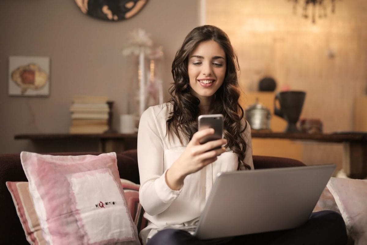 woman sitting on sofa while looking at phone with laptop on 920382