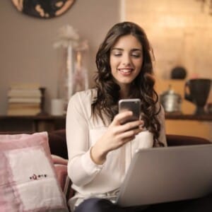 woman sitting on sofa while looking at phone with laptop on 920382